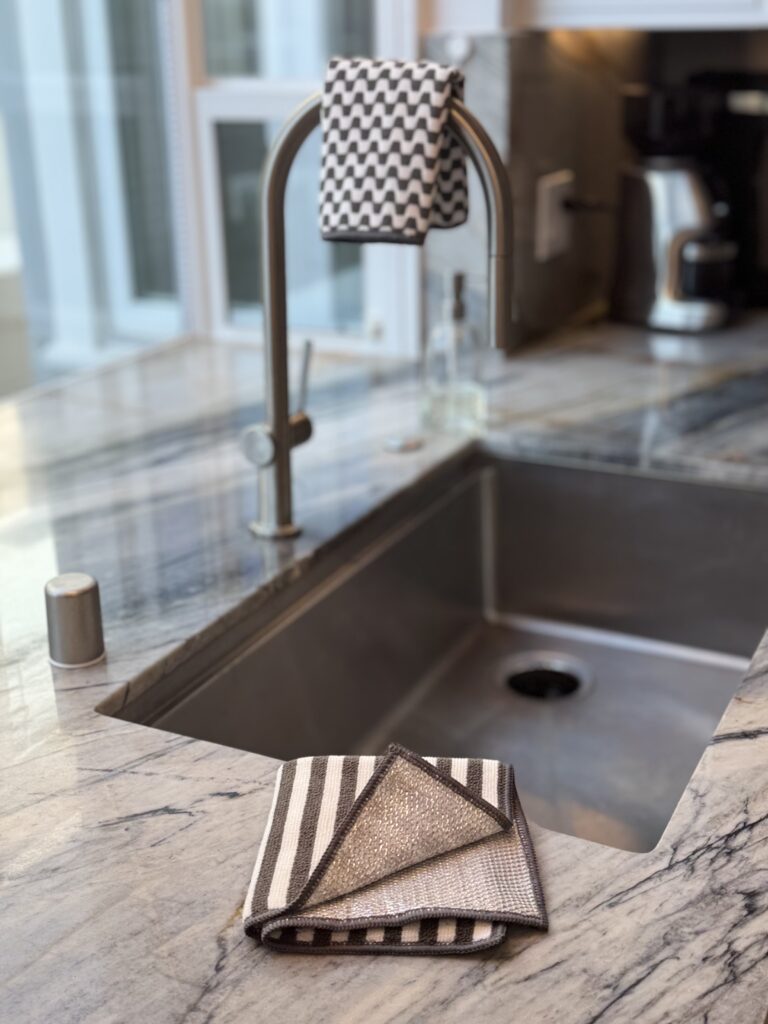 Severn Dish Cloth folded beside a kitchen sink, showing dual-sided microfiber and non-scratch scrubbing surface in a modern kitchen