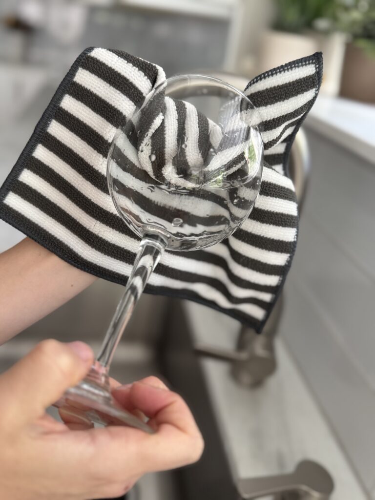 Person using the eco-friendly Severn Dish Cloth to clean a wine glass, showing a reusable kitchen cloth that leaves glassware streak-free and spotless.