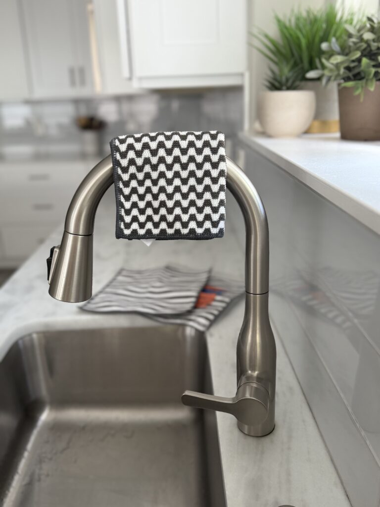 The Severn Dish Cloth, part of a minimalist kitchen essentials, laid across sink faucet next to clean white countertops arranged in an organized, clutter-free style.