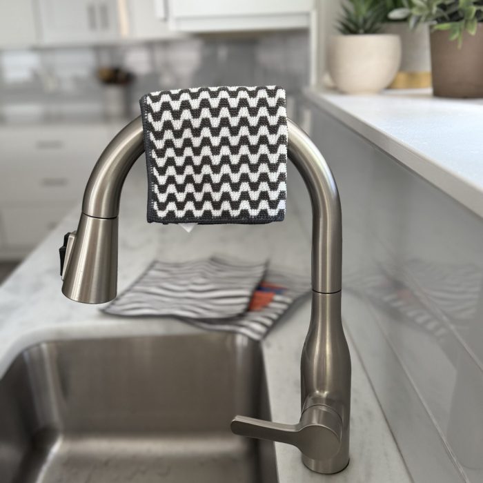The Severn Dish Cloth, part of a minimalist kitchen essentials, laid across sink faucet next to clean white countertops arranged in an organized, clutter-free style.