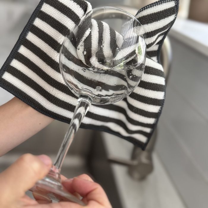 Person using the eco-friendly Severn Dish Cloth to clean a wine glass, showing a reusable kitchen cloth that leaves glassware streak-free and spotless.